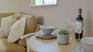 A living room with a sofa, a table with a bowl, a succulent plant, wine glasses, and a bottle. - 1 bedroom accommodation in Towyn, near Rhyl (Towyn, near Rhyl)