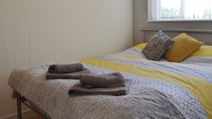 A neatly made bed with rolled towels, a patterned bedspread, and a window with a view. - 1 bedroom accommodation in Towyn, near Rhyl (Towyn, near Rhyl)
