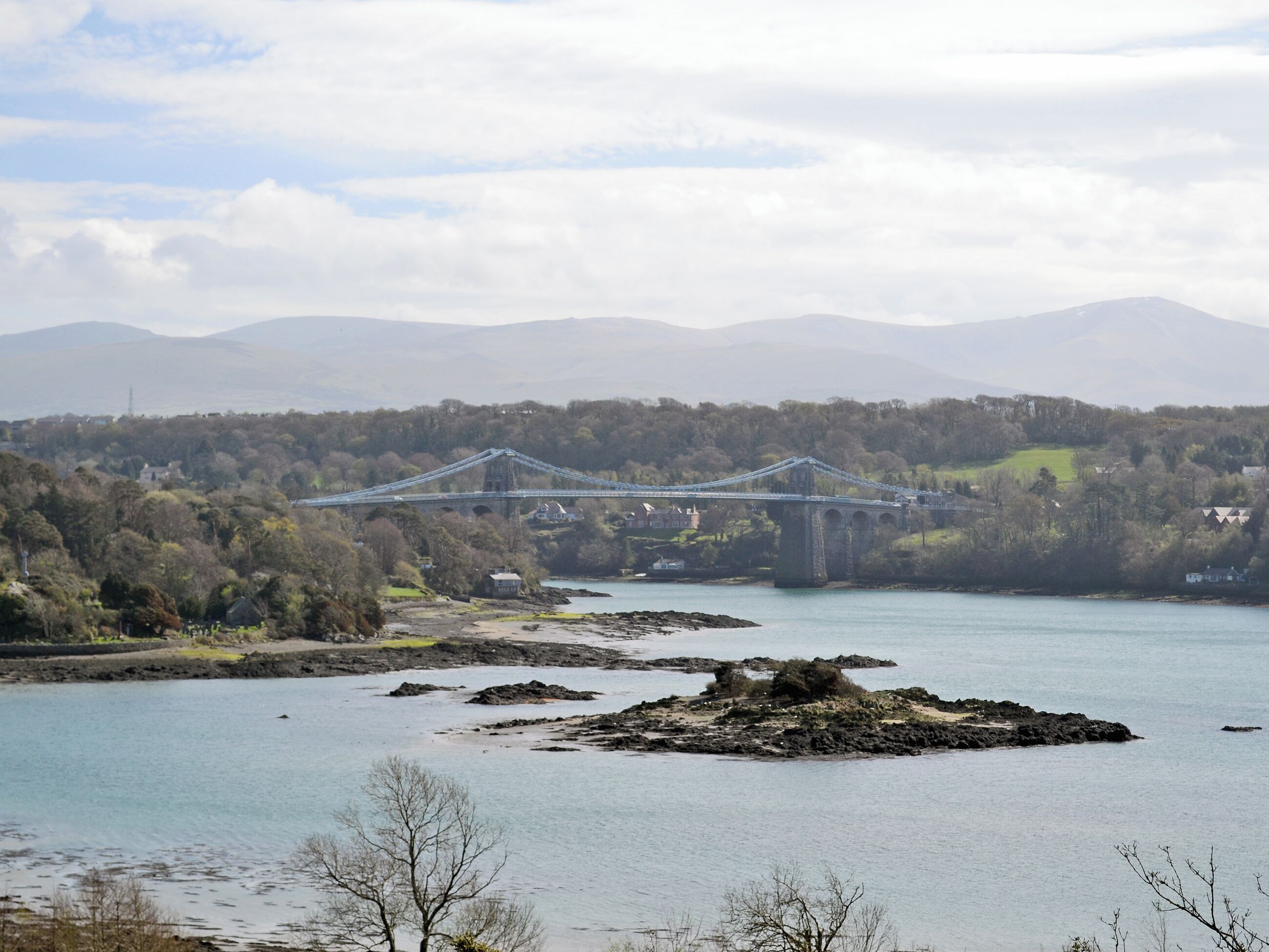 A bridge over a river with surrounding hills and sparse vegetation.