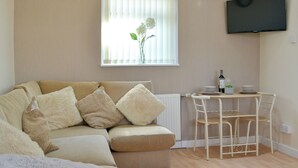 A living room with a sofa, a small table with a bottle and glasses, a radiator, and a TV mounted on the wall. - 1 bedroom accommodation in Towyn, near Rhyl (Towyn, near Rhyl)