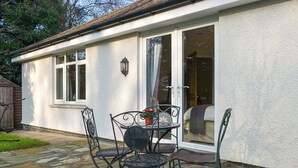 Ein kleines Haus mit einer Terrasse, komplett mit Tisch, Stühlen, einer Topfpflanze und einem Vogelbad.