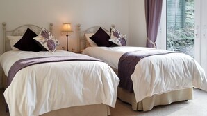 Ein Doppelzimmer mit zwei Betten, jeweils mit Kopfteil, Nachttischlampe und einem Vorhangfenster.
