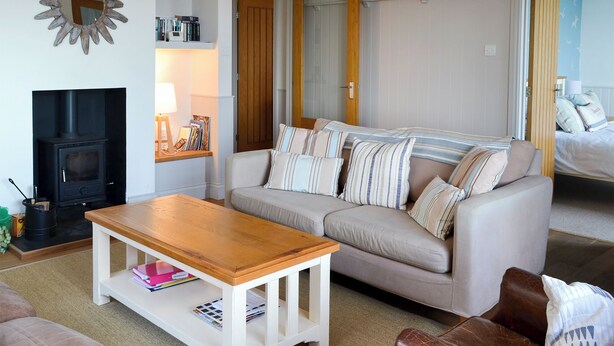 A living room with a sofa, a wooden coffee table, a fireplace, and a bookshelf. - 3 bedroom accommodation in Beadnell (Beadnell)