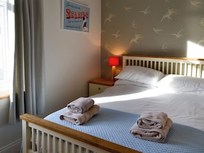 A neatly made bed with folded towels, a bedside lamp, and a wall sign with a bird motif.