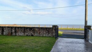 A paved pathway leading to a stone wall with a metal gate, overlooking a coastal area with a fence and a clear sky. - 3 bedroom accommodation in Beadnell (Beadnell)
