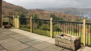 A balcony with a stone bench, a potted plant, and a view of a hilly landscape.