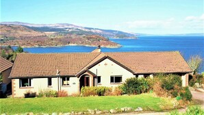 A house with a tiled roof, a small porch, and a view of a lake and mountains in the background.