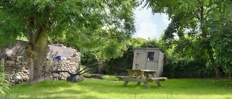 A rustic outdoor setting with a wooden shed, a picnic table, and a stone wall.