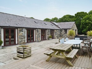 Un bâtiment en pierre doté d’un patio carrelé, d’une table de pique-nique en bois et d’un espace extérieur aménagé pour s’asseoir.