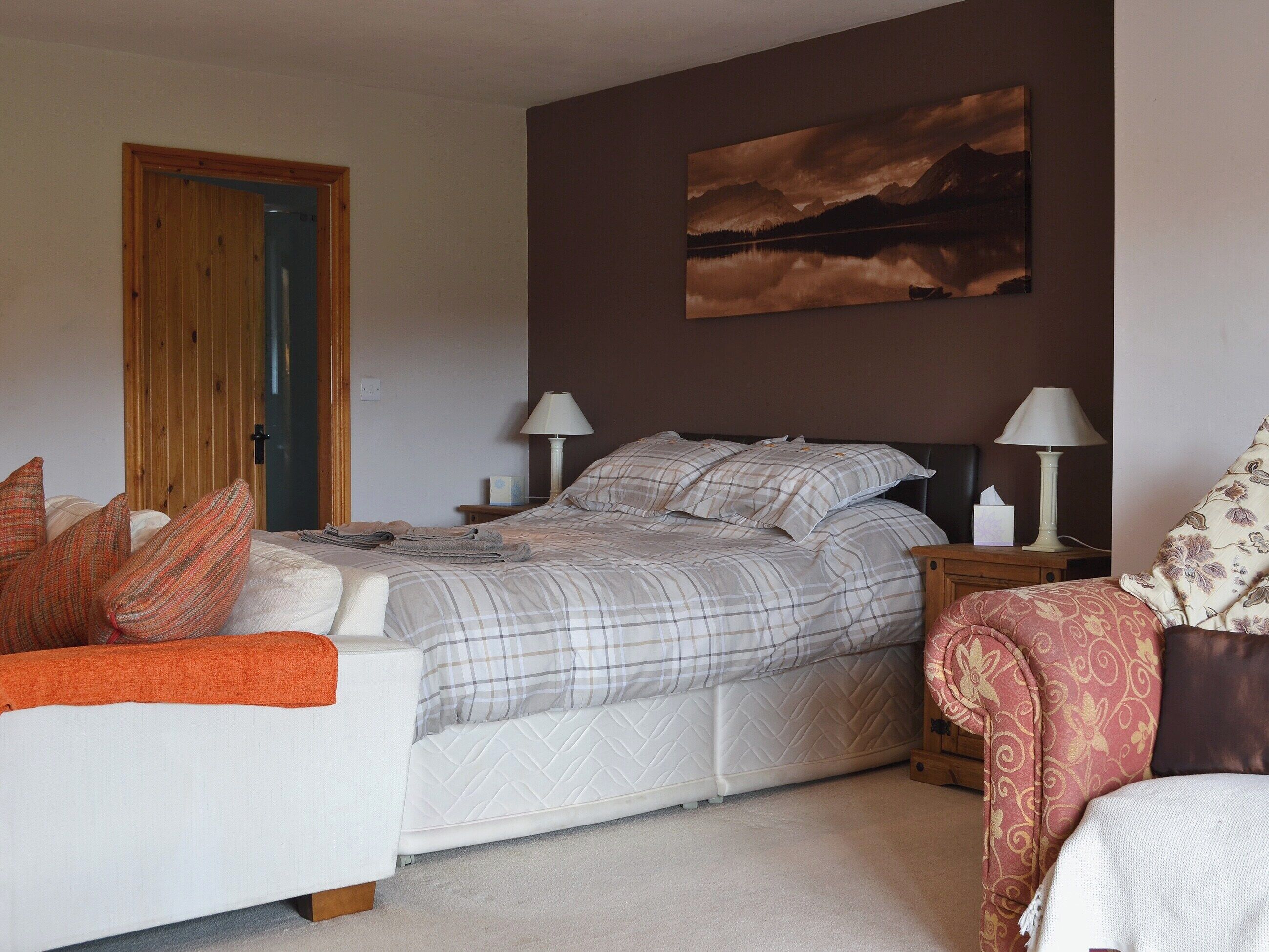 Un dormitorio con cama, dos mesitas de noche con lámparas, una puerta de madera y un cuadro en la pared.