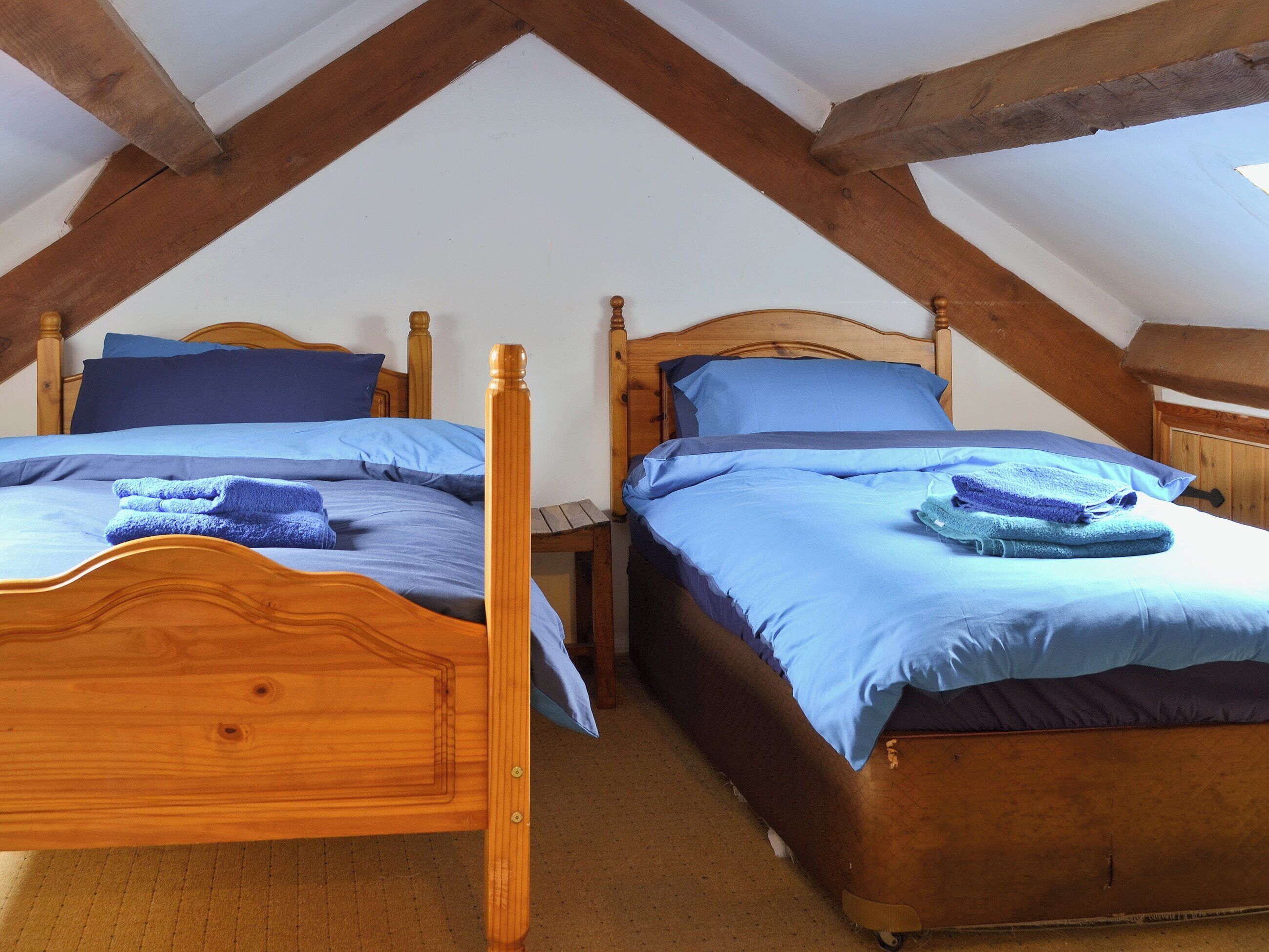Two wooden beds with blue bedding in a room with exposed wooden beams.