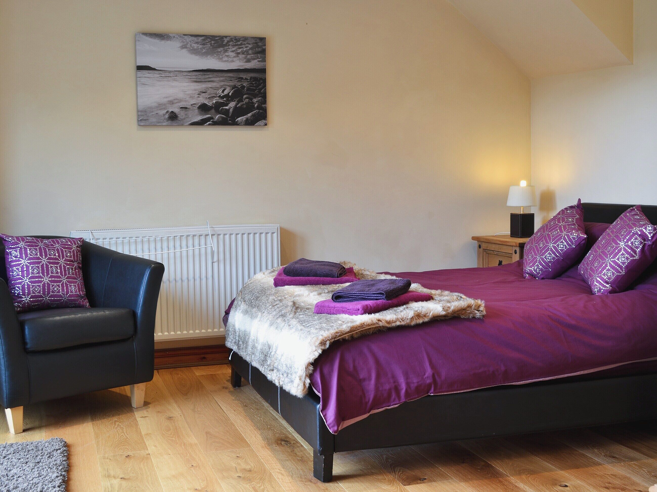 Une chambre à coucher comprenant un lit, une chaise, un radiateur, une table de chevet et une lampe.