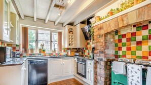 A kitchen with white cabinets, a tiled backsplash, a brick oven, and a window with curtains. - 4 bedroom accommodation in Rosedale Abbey (Rosedale Abbey)