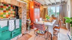 A kitchen with a brick wall, colorful tiles, a green stove, and a dining area with a table and chairs. - 4 bedroom accommodation in Rosedale Abbey (Rosedale Abbey)