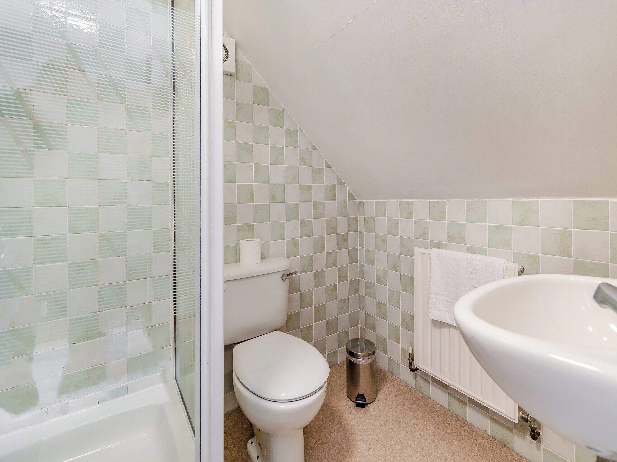 A small bathroom with a toilet, a trash can, a sink, and a shower.