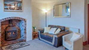 Ein Wohnzimmer mit Kamin aus Ziegelsteinen, einer Couch, einem Sessel, einer Stehlampe und einem Spiegel an der Wand.