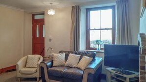 Ein Wohnzimmer mit einer Couch, einem Sessel, einem Fernseher und einem Fenster mit Vorhängen.