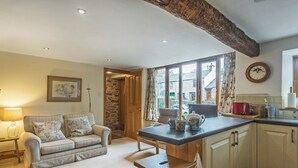 A cozy living room with a sofa, a coffee table, and a kitchen area with a bar stool. - Castle House Cottage (Hartley, near Kirkby Stephen)