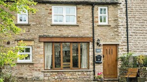 A stone building with a wooden door, a bench, and a sign reading "Castle House Cottage." - Castle House Cottage (Hartley, near Kirkby Stephen)
