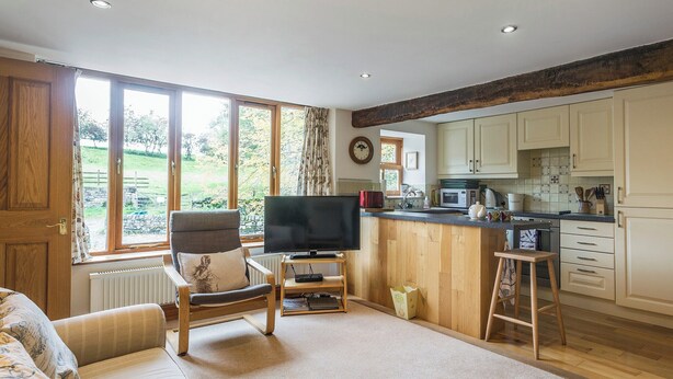A cozy living room with a sofa, a TV, and a wooden-framed window. - Castle House Cottage (Hartley, near Kirkby Stephen)