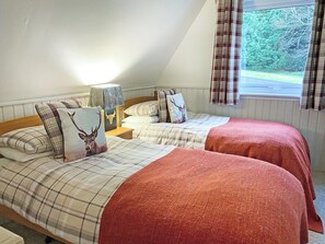 Une chambre avec deux lits, une literie à motifs écossais, une lampe et une fenêtre avec des rideaux.
