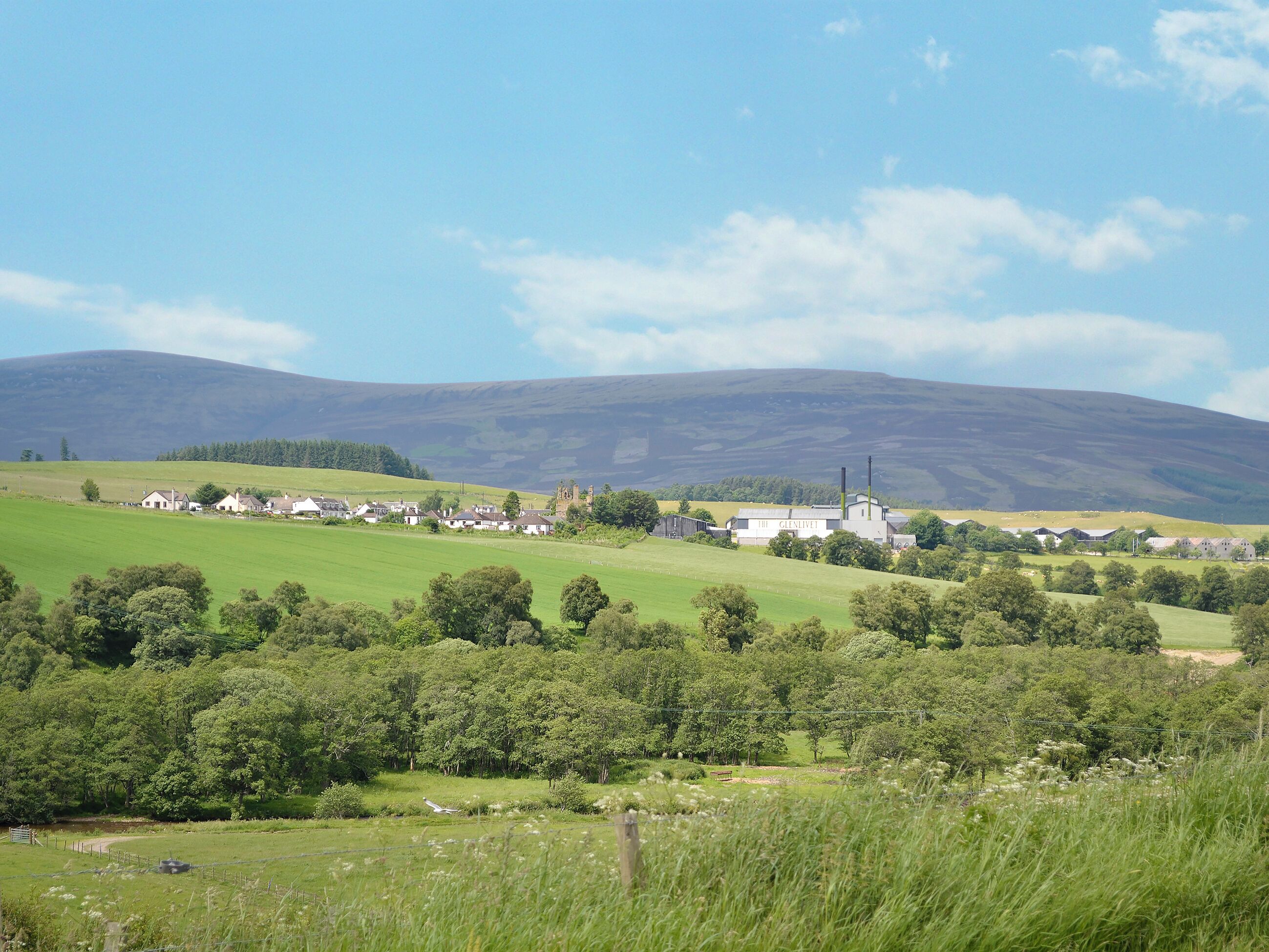 Ländliche Landschaft mit sanften Hügeln, einem kleinen Dorf und einem markanten Gebäude mit der Aufschrift 'THE GLENIVEIL'.