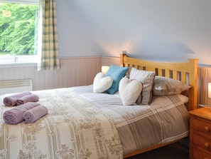 A neatly made bed with a floral-patterned bedspread, a wooden headboard, and several pillows, including heart-shaped ones.