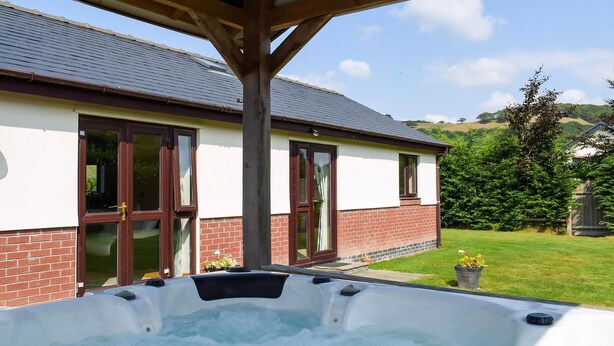 A hot tub under a wooden pergola with a house in the background.