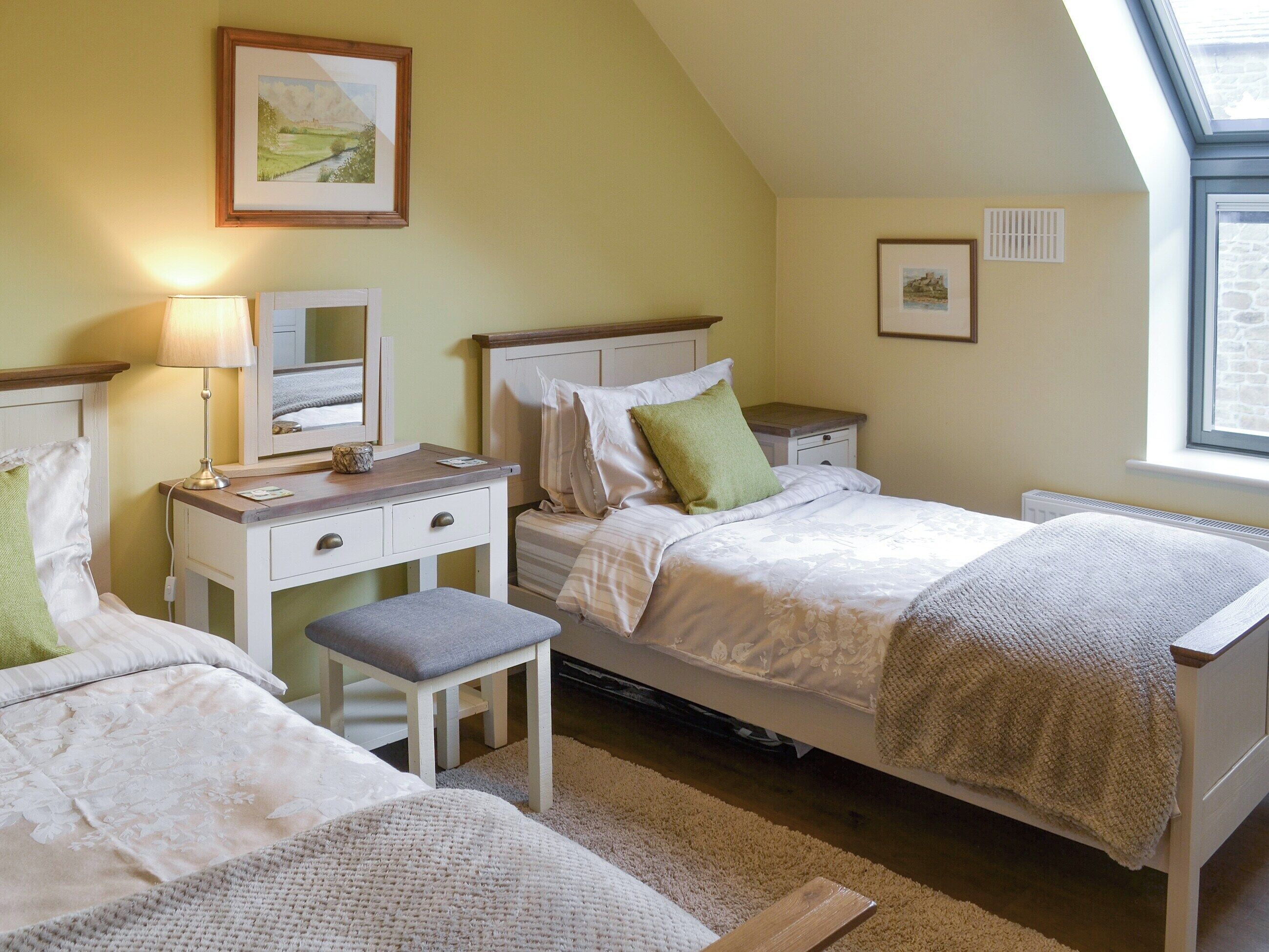 A bedroom with two beds, a desk, a chair, and a window.
