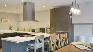 Una cocina moderna con una isla central, taburetes de bar, una mesa de comedor y un horno empotrado.