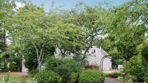 Ein Garten mit Kiesweg, verschiedenen Sträuchern und einem Steinhaus im Hintergrund.