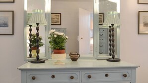 A white dresser with two mirrors, two lamps, and a potted plant.