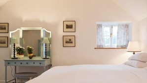 A bedroom with a bed, a dresser with a mirror, a window with curtains, and framed pictures on the wall.