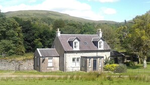 A stone house with a large front yard and a view of hills in the background.