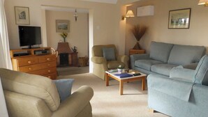 A living room with a sofa, armchairs, a coffee table, a fireplace, and a television. - 2 bedroom accommodation in Otterton (Otterton)