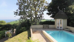 A pool area with a view of the sea, surrounded by greenery and a small gazebo. - 2 bedroom accommodation in Otterton (Otterton)