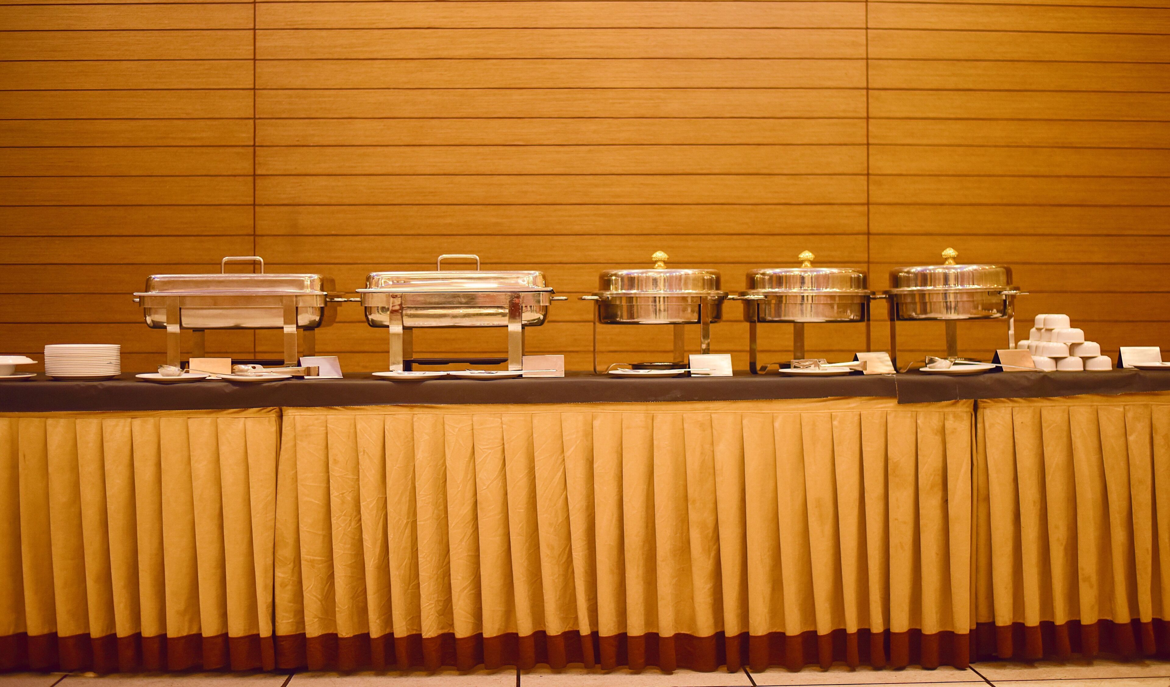 A buffet setup with multiple serving stations, each with a covered food container and a stack of white plates.
