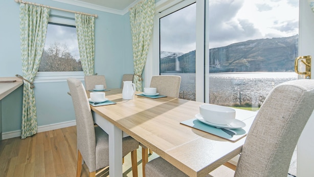 Un espace repas comprenant une table, des chaises et offrant une vue sur un lac et des montagnes.