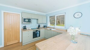 Une cuisine moderne avec une porte en bois, un four à micro-ondes, un évier et une fenêtre donnant sur des arbres.