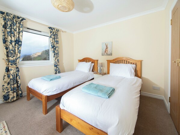 A room with two wooden beds, a window with curtains, a painting on the wall, and a door. - 3 bedroom accommodation in Inverinate, by Kyle (Inverinate, by Kyle)