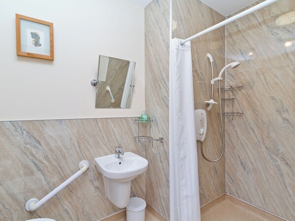 Baño con pared de mármol, lavamanos, ducha, un cuadro enmarco y pasamanos.