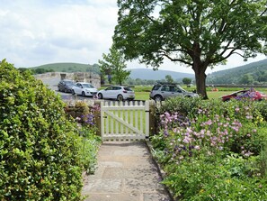 A stone pathway leading to a gated entrance with parked cars and a tree-lined view.