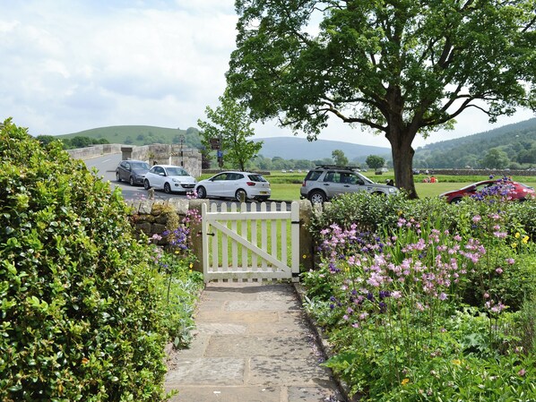 A stone pathway leading to a gated entrance with parked cars and a tree-lined view.