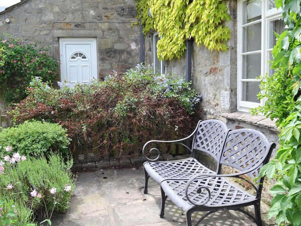 A stone building with a white door, a bench, and various plants.