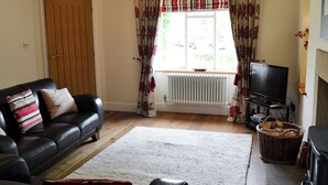 A living room with a sofa, a television, a fireplace, and a window with curtains. - 3 bedroom accommodation in Burnsall (Burnsall)