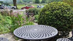 A garden with a round metal table and chairs, surrounded by greenery and flowers. - 3 bedroom accommodation in Burnsall (Burnsall)