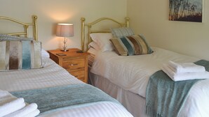 A hotel room with two beds, a nightstand with a lamp, a wooden drawer, and a painting on the wall. - 3 bedroom accommodation in Burnsall (Burnsall)