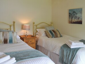 A hotel room with two beds, a nightstand with a lamp, a wooden drawer, and a painting on the wall.