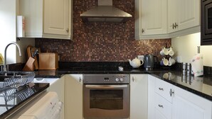 A kitchen with white cabinets, a stainless steel oven, a black countertop, and a tiled backsplash. - 3 bedroom accommodation in Burnsall (Burnsall)