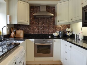 A kitchen with white cabinets, a stainless steel oven, a black countertop, and a tiled backsplash.